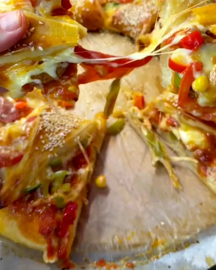 Golden braided crown pizza with bubbling cheese and sesame seeds on a baking sheet