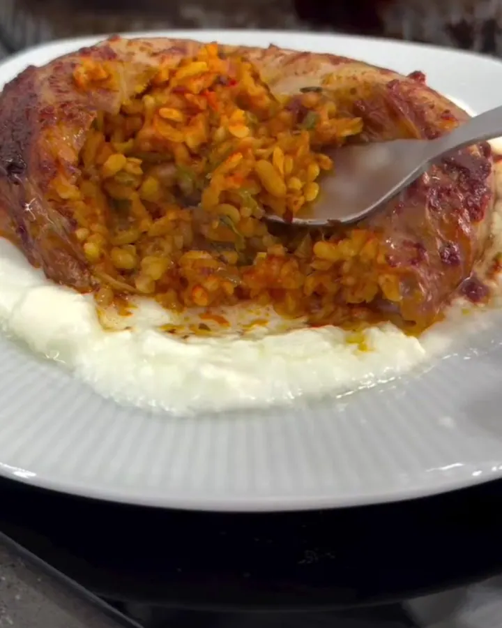 Roasted cabbage parcel sliced open, showing spiced beef and rice filling on a bed of garlic yogurt