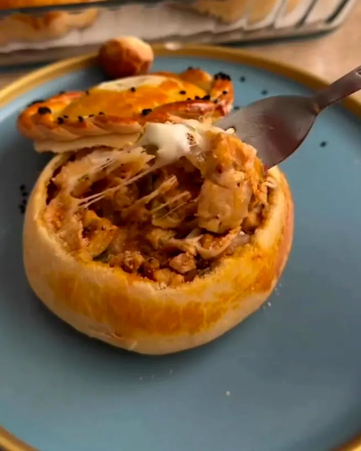 Golden braided pastry pot with steam rising as the lid is lifted, revealing melted cheese and chicken.