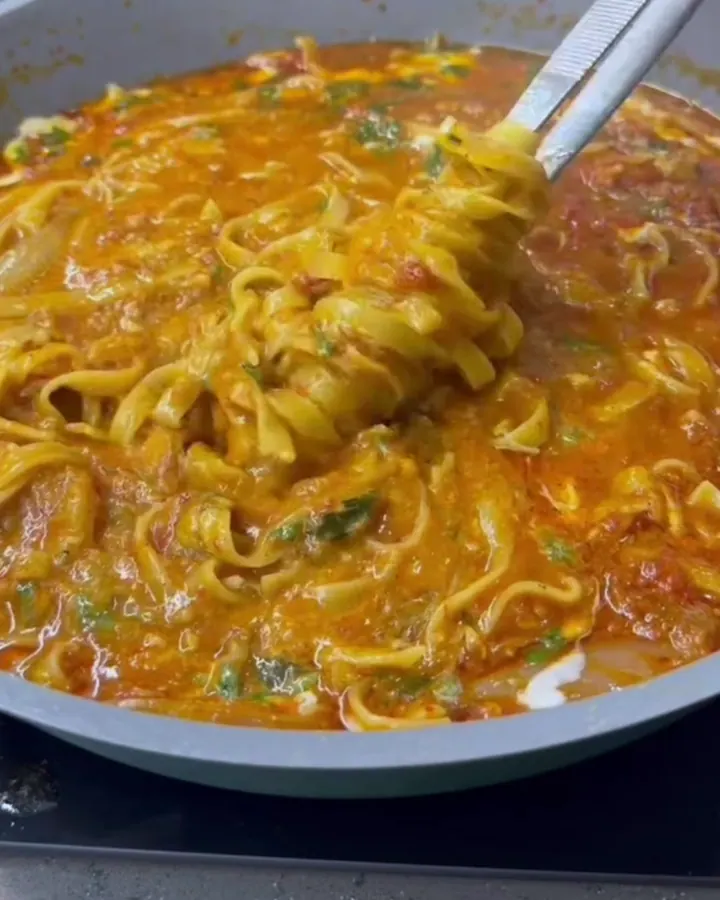 Twirled tagliatelle with roasted vegetables and melted mozzarella in a wide ceramic bowl