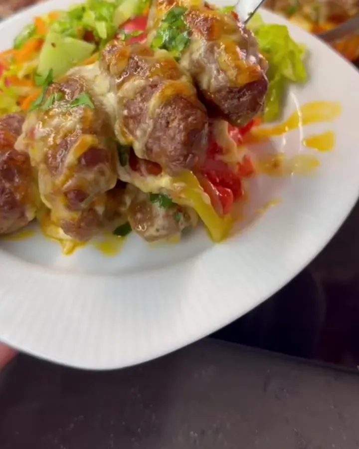 Golden cheese-crusted meatballs with roasted peppers in a baking dish