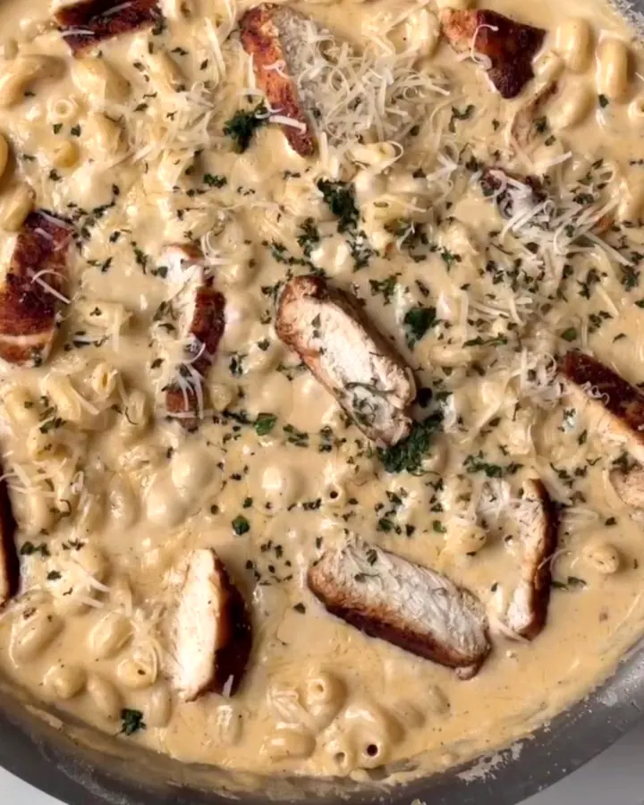 Spoon lifting a cheesy, chicken-topped mac and cheese with a long cheese pull