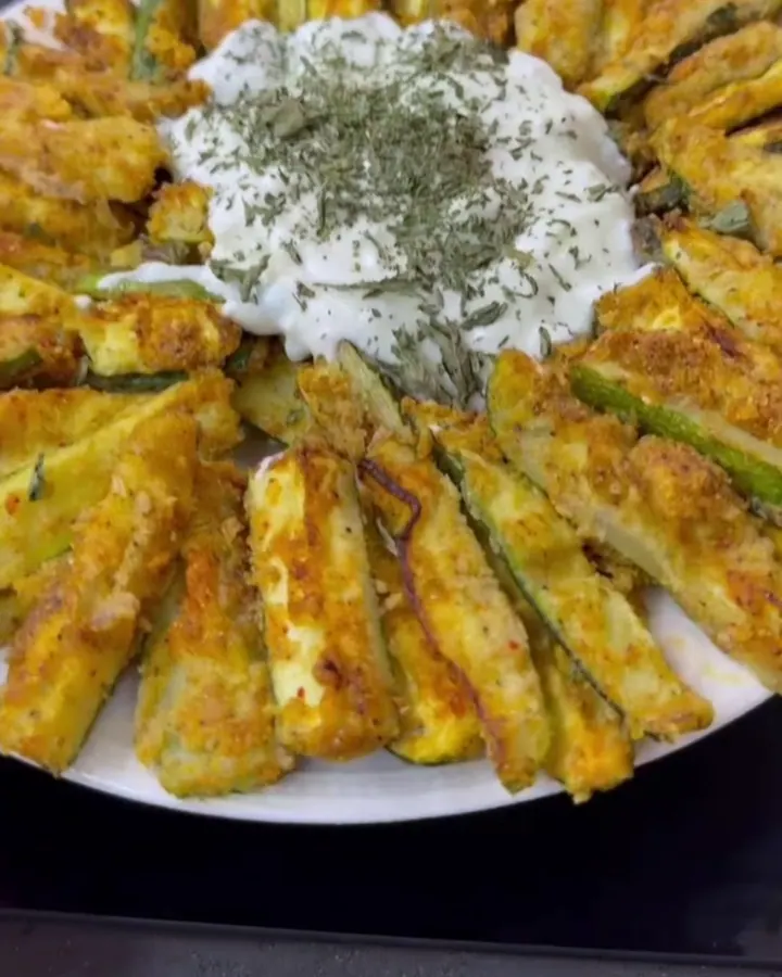 Crispy baked zucchini fries with a golden crust, served with a bowl of garlic herb yogurt dip.