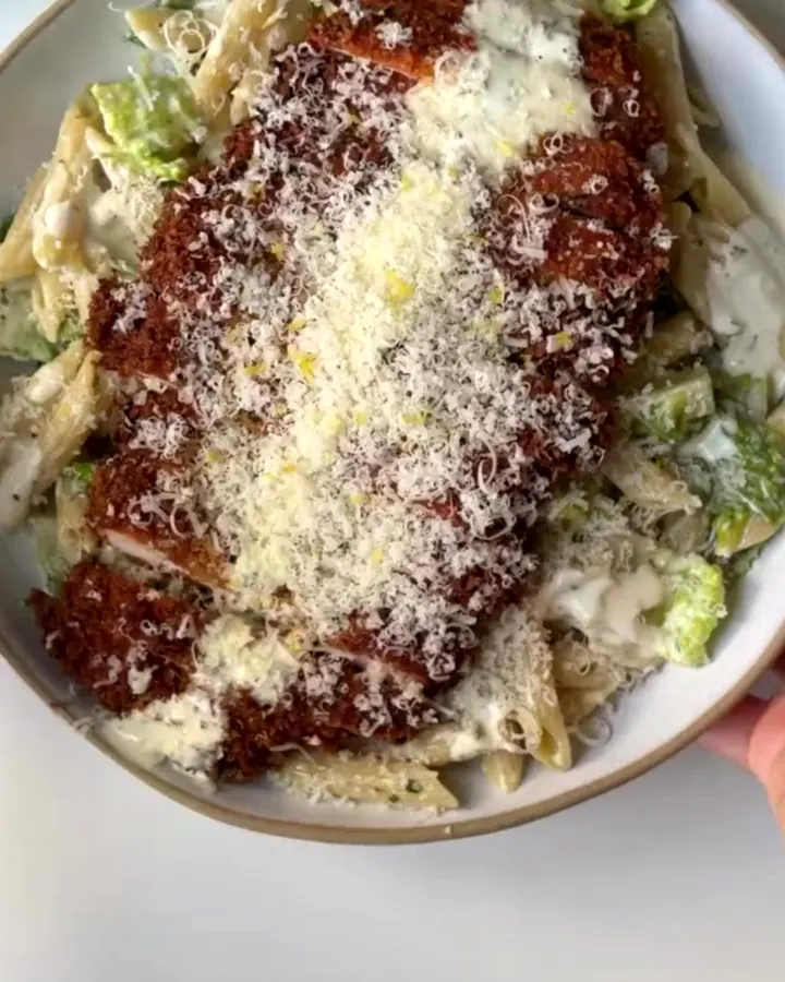 Golden fried chicken strips on top of creamy pasta salad with romaine and Parmesan