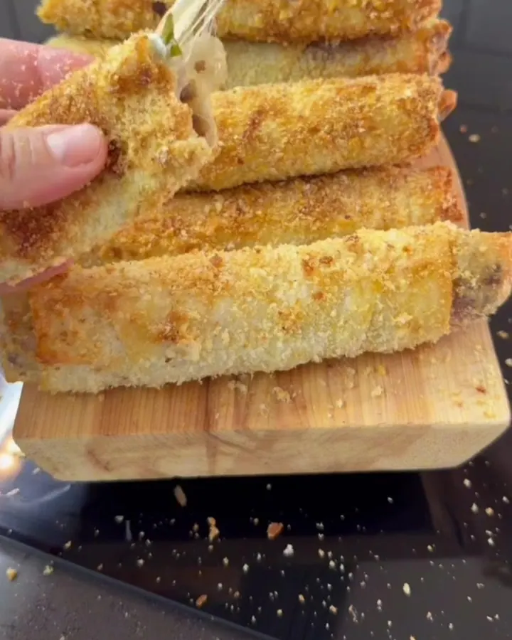 Golden paçanga rolls on a parchment-lined baking sheet, one snapped in half showing melted cheese and pastırma.