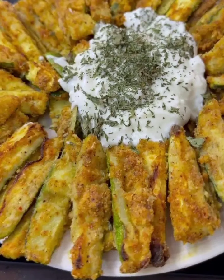 Crispy roasted zucchini fries with garlic yogurt sauce, one being dipped.