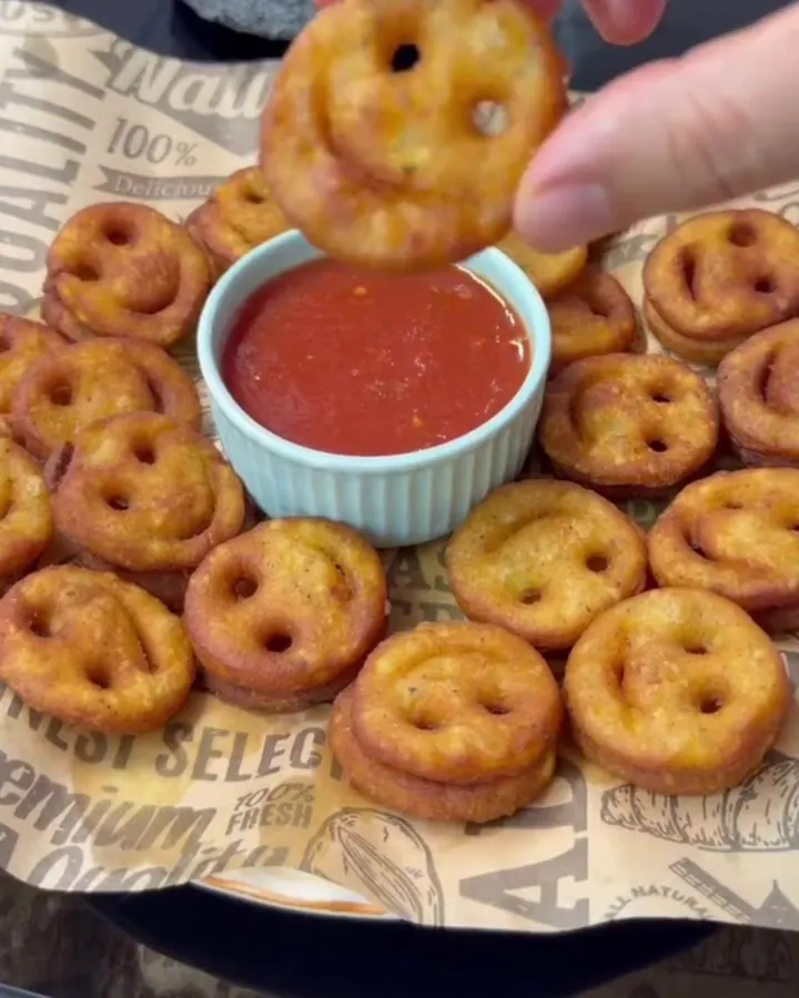 Crispy smiley potato fries piled on a plate with a small bowl of ketchup