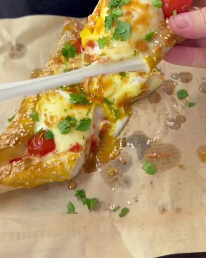 A golden lavaş breakfast boat sliced in half, with molten cheese pulling and a glossy egg yolk visible.