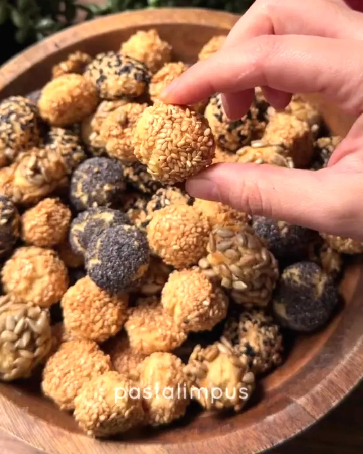 Golden sesame marble crackers piled in a ceramic bowl, with one cracked open showing crumbly texture