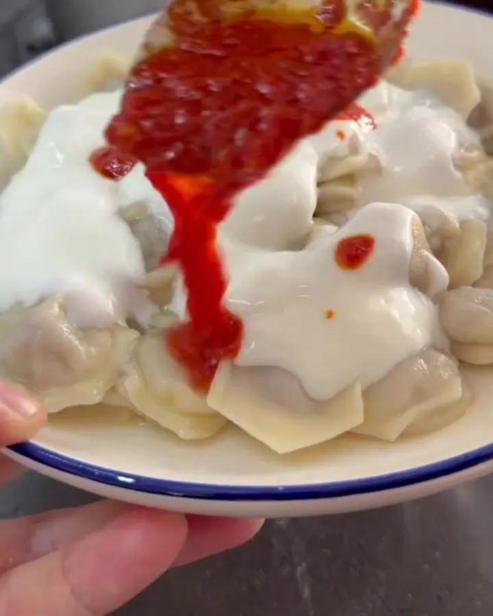 Cooked mantı dumplings on a ceramic dish topped with garlic yogurt and sizzling butter