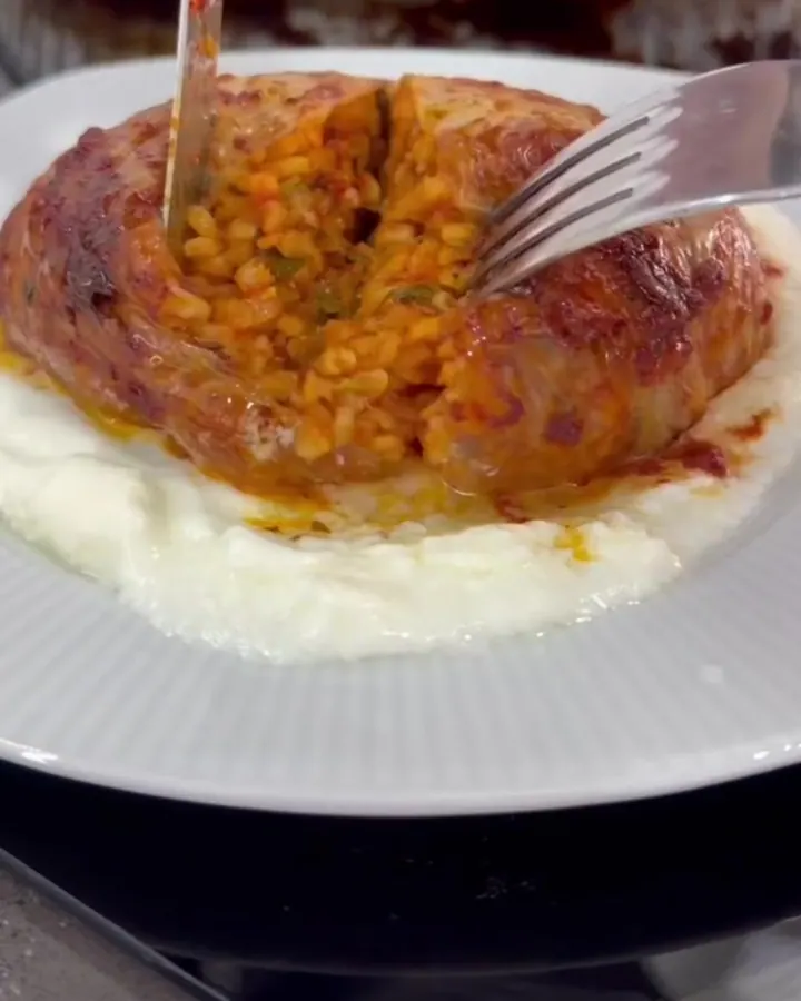 A spatula lifting a glistening stuffed cabbage roll from a baking dish, with translucent leaves and savory juices.