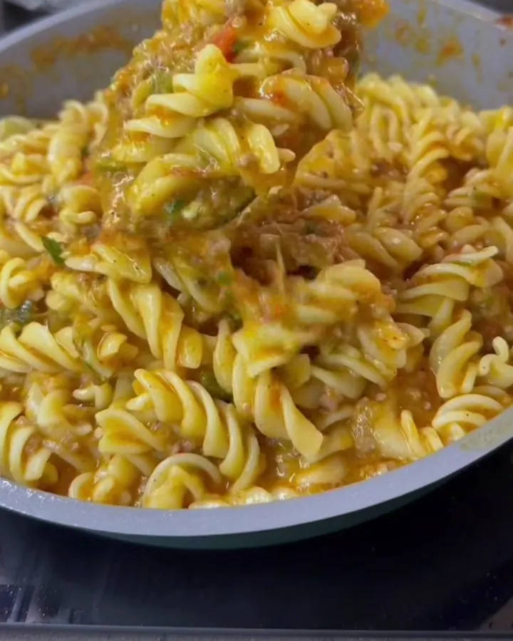 A fork twirls a large spoonful of spiral fusilli with braised tomato sauce, roasted eggplant, and meatball on a plate.