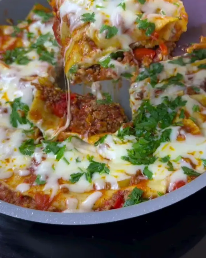 A spatula lifting a cheesy slice of skillet lasagna with a long mozzarella pull