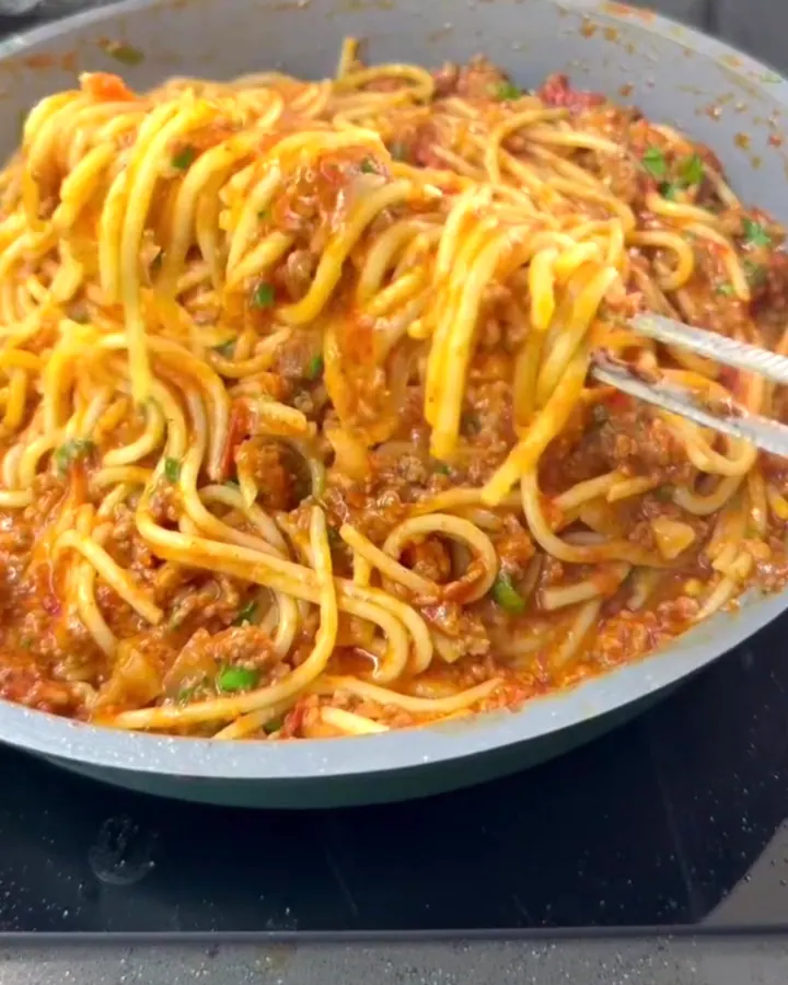 A fork twirling spaghetti with tomato beef sauce, topped with Parmesan and basil