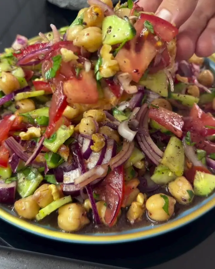 A fork piling vibrant chickpea salad onto a golden toasted baguette slice, with pomegranate juices glistening.