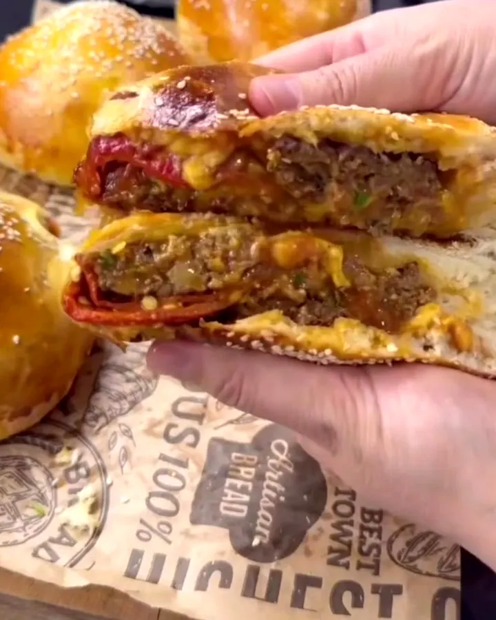 Pull-apart cheeseburger bun bomb with golden crust and sesame seeds, torn open to show melted cheddar and juicy beef.