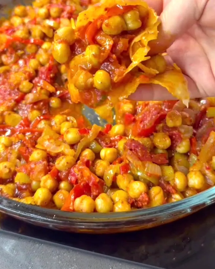 A scoop of roasted chickpea casserole with peppers and tomatoes, held over the dish.