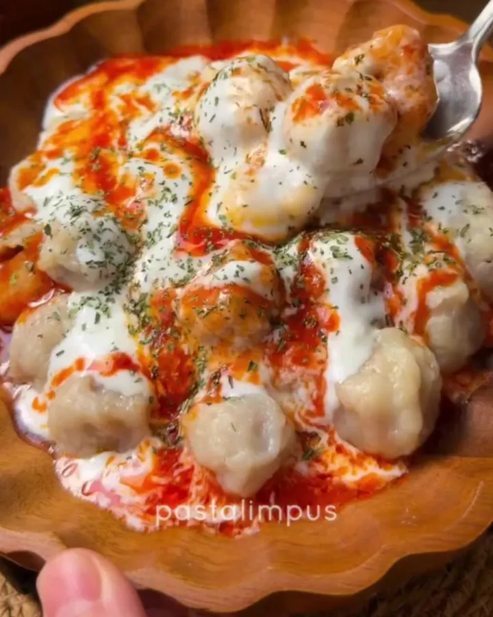 A plate of tiny dumplings topped with garlic yogurt and a drizzle of chili butter, garnished with fresh parsley.